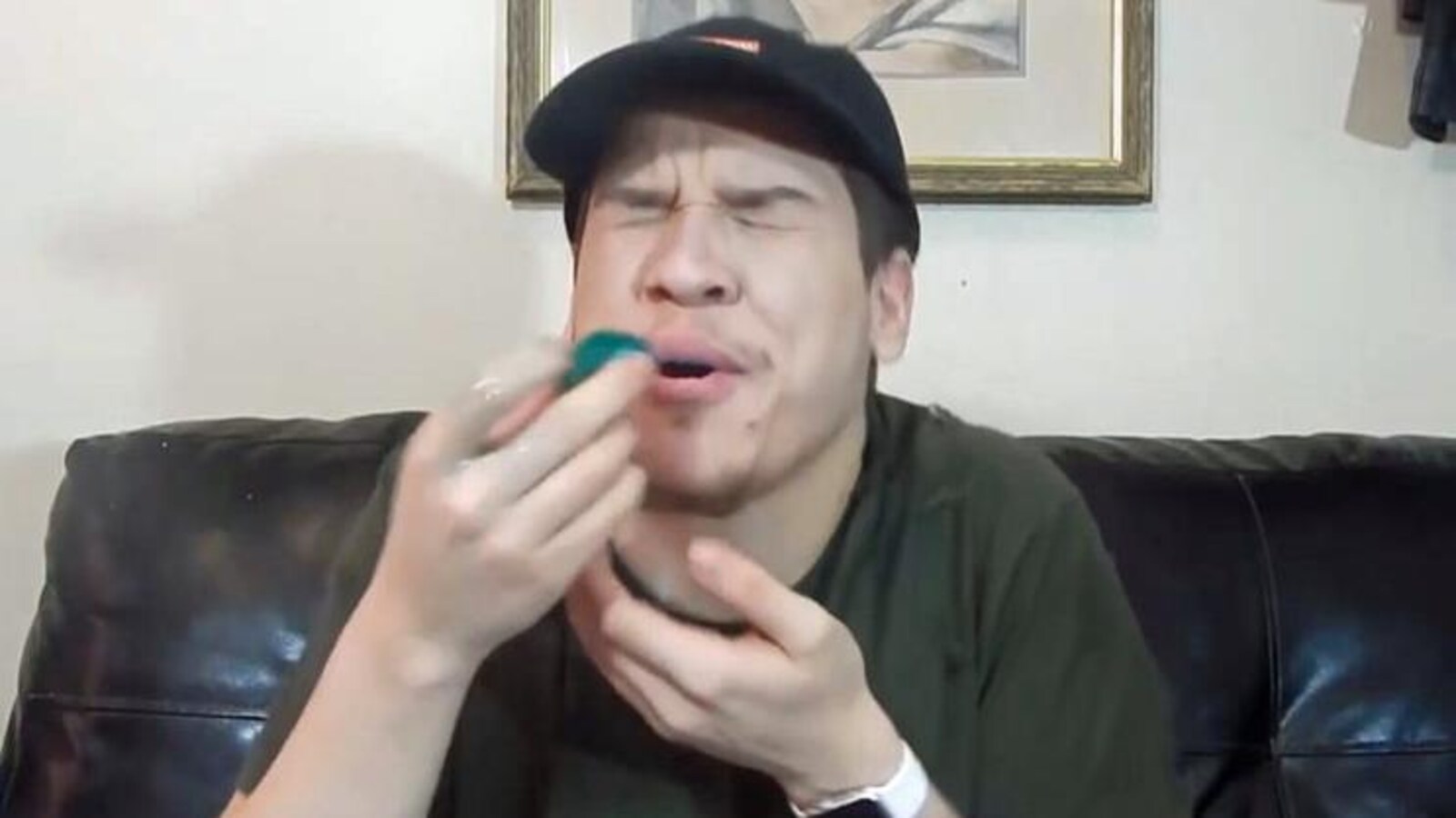 Un jeune homme assis sur un canapé s'apprête à mettre dans sa bouche une capsule de lessive en gel.