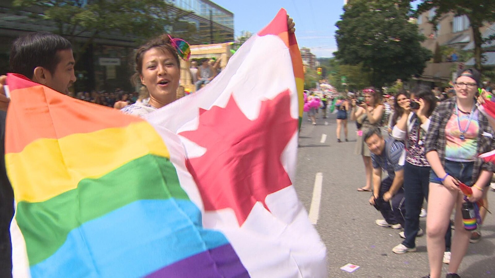 Une femme brandit le drapeau du Canada orné des couluers de la fierté gaie.
