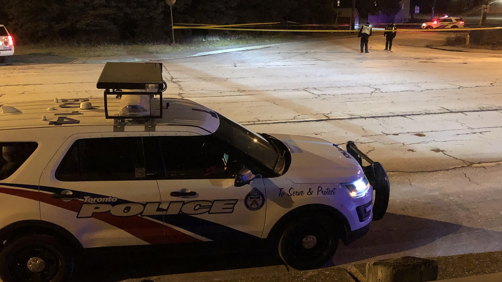 Photo d'un véhicule de police et d'une banderole jaune bloquant une rue. Deux policiers sont en arrière-plan.
