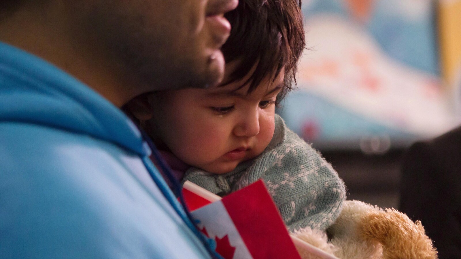 Une petite fille dans les bras de son père qui tient un petit drapeau canadien