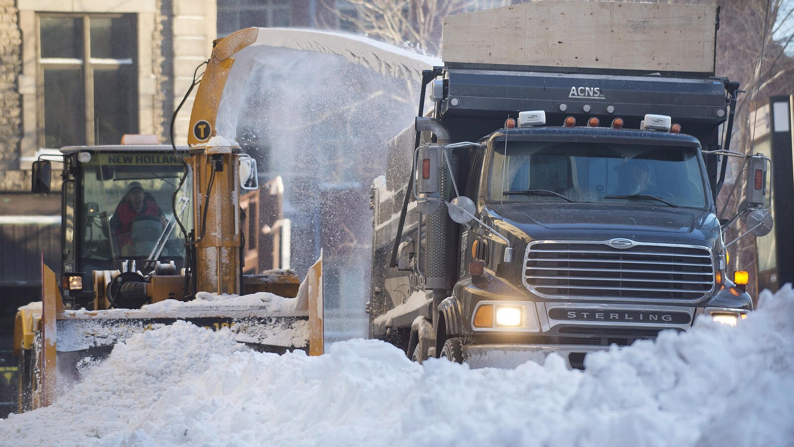 Un déneigeur souffle de la neige dans un camion de chargement, à ses côtés.