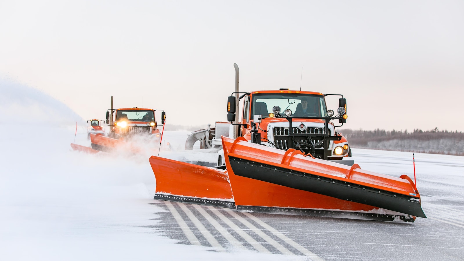 Deux déneigeuses orange s'activent à retirer la neige sur l'une des pistes de l'aéroport de Charlottetown.