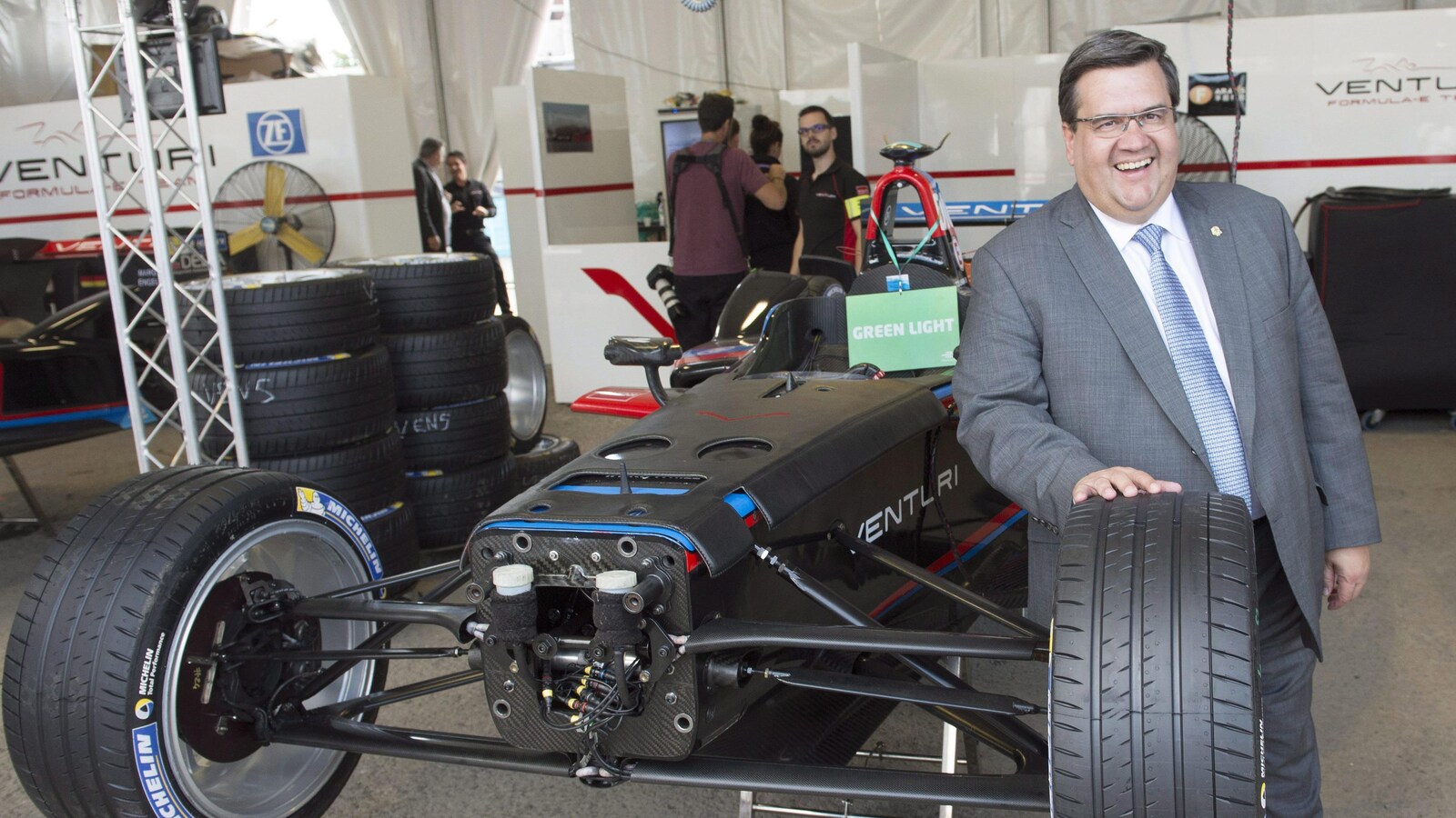 M. Coderre se tient debout à côté d'une voiture de course, posant la main sur l'un de ses pneus.