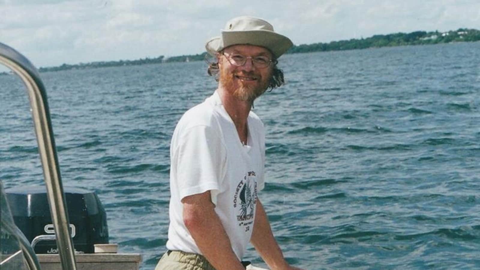 On voit le professeur sur un bateau vétu d'un chapeau et de lunettes de vue.
