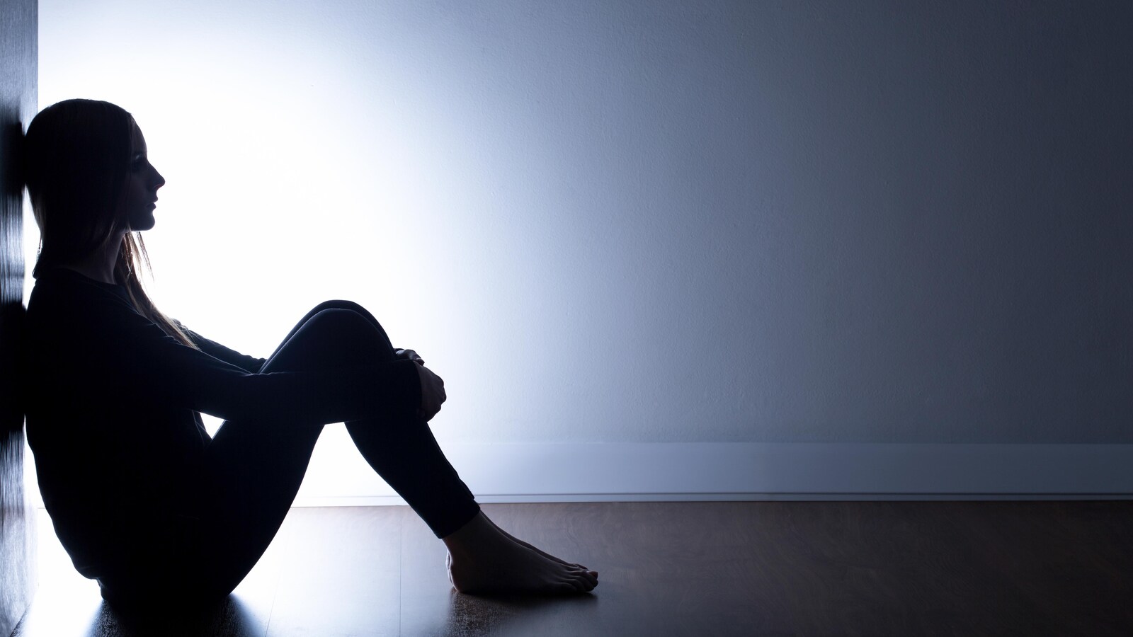 Une jeune fille assise au sol et adossée à un mur, dans l'obscurité.