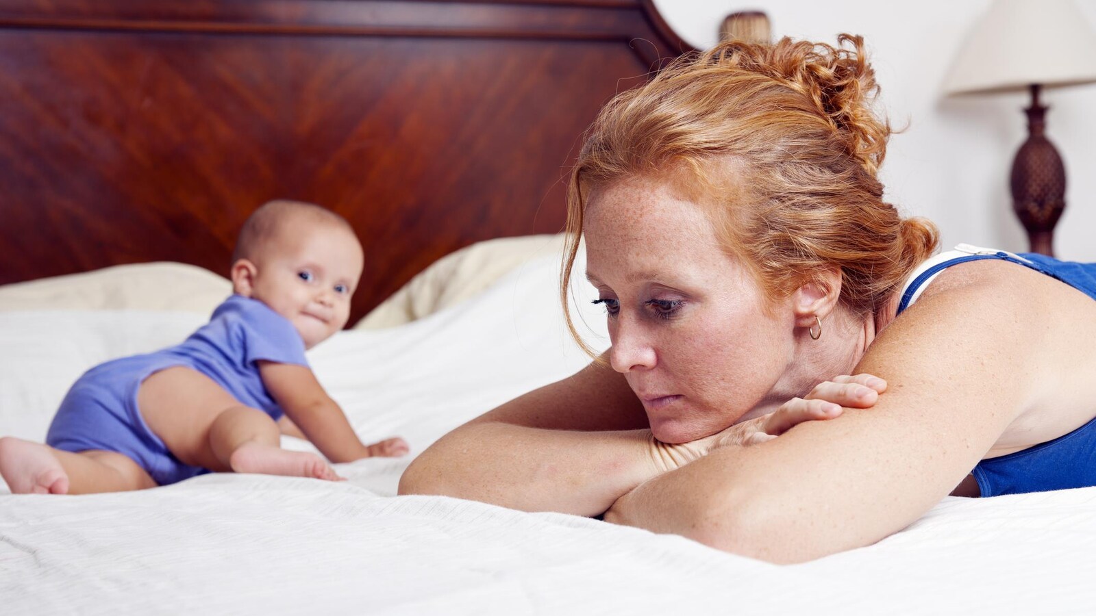 Une mère est couchée sur un lit avec son enfant, mais semble perdue dans ses pensées.