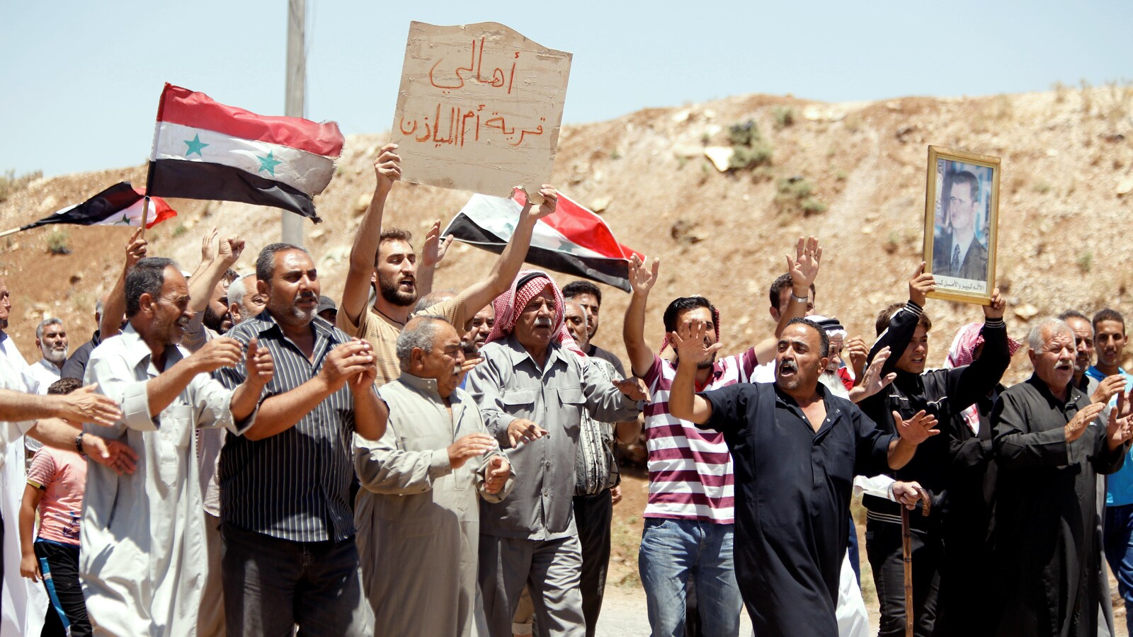 Les habitants d’Oum Al-Mayazen, banlieue de Deraa, tiennent des drapeaux syriens et le portrait du président syrien Bachar Al-Assad.