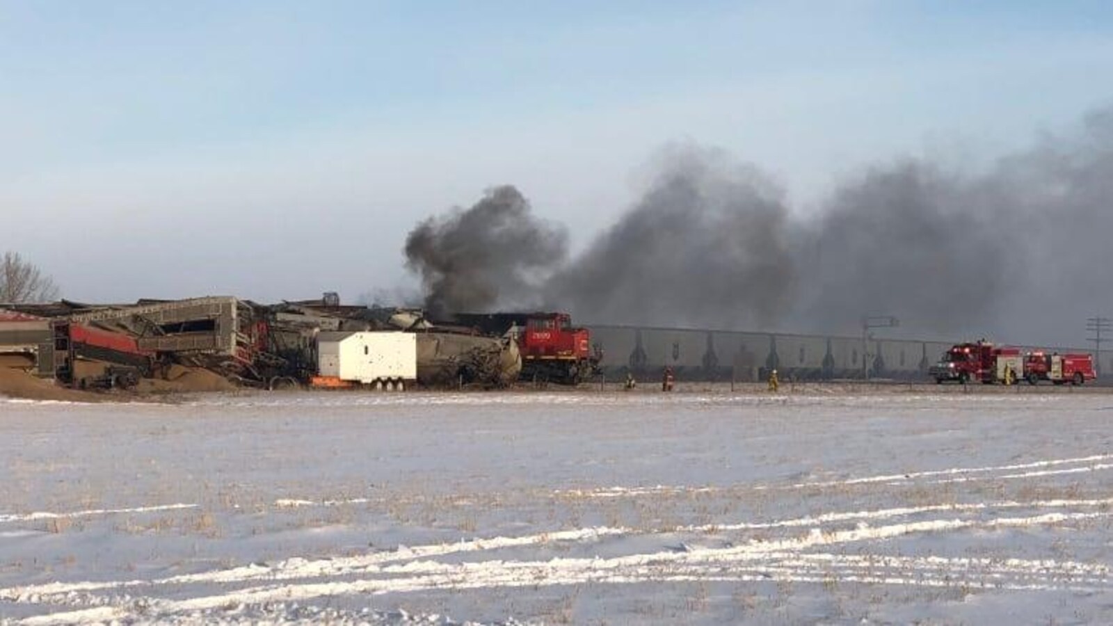 La fumée s'échappe des wagons abîmés du train, deux camions de pompiers s'approchent du train.