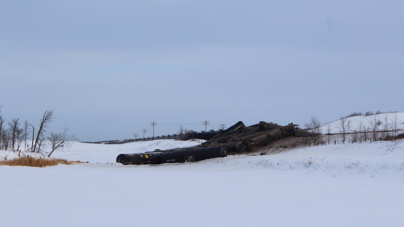 Le déraillement de train, vu de loin : on voit des wagons empilés les uns sur les autres dans un champ recouvert de neige.