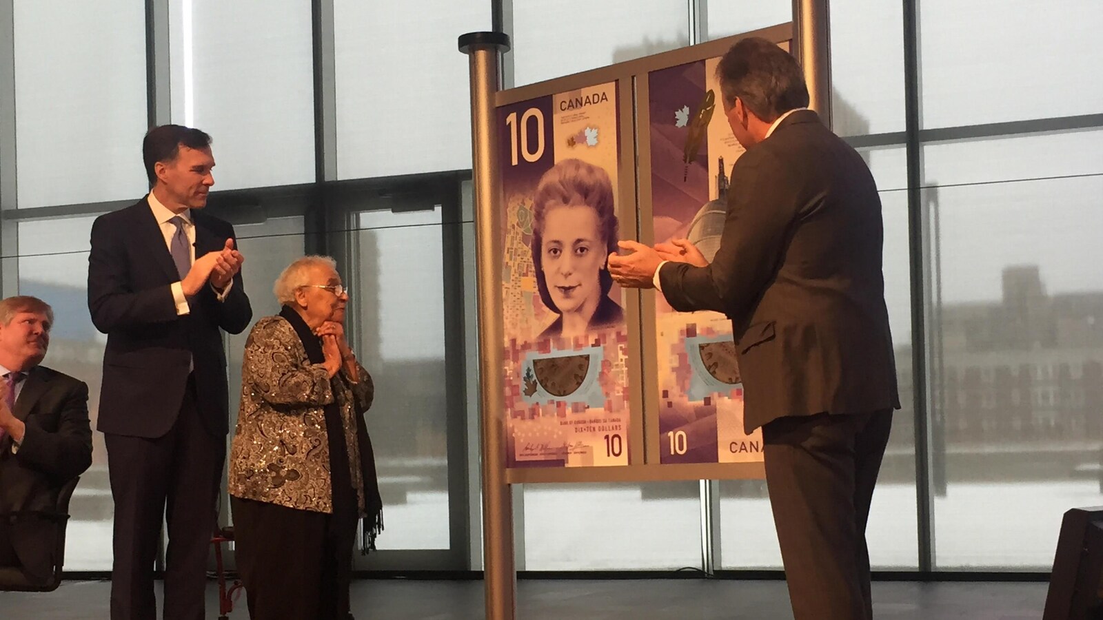 Des dignitaires entourent une grande affiche illustrant le nouveau billet de banque de 10 $.