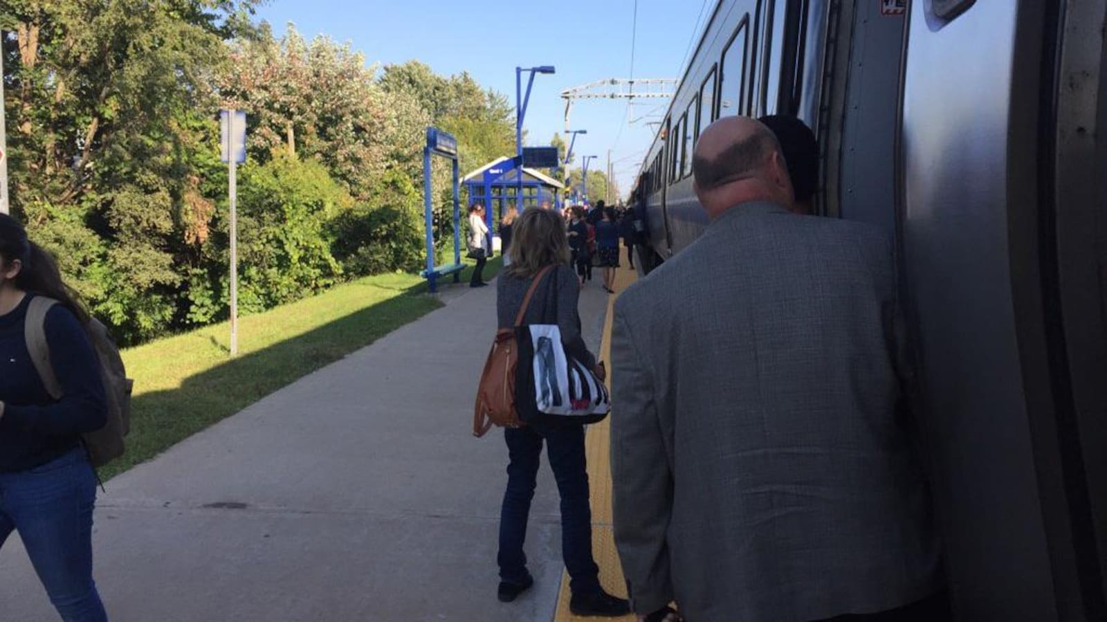 Une femme et un homme, en avant-plan, sont photographiés en train de descendre d'un train de banlieue.