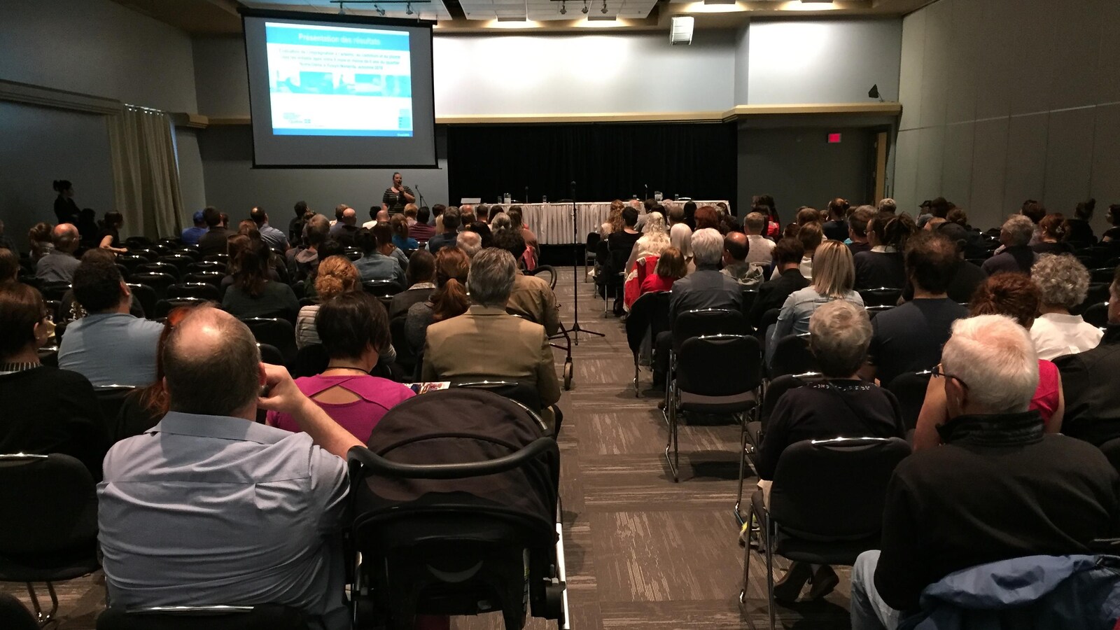 Plusieurs dizaines de citoyens écoutent une présentation dans une salle de congrès.