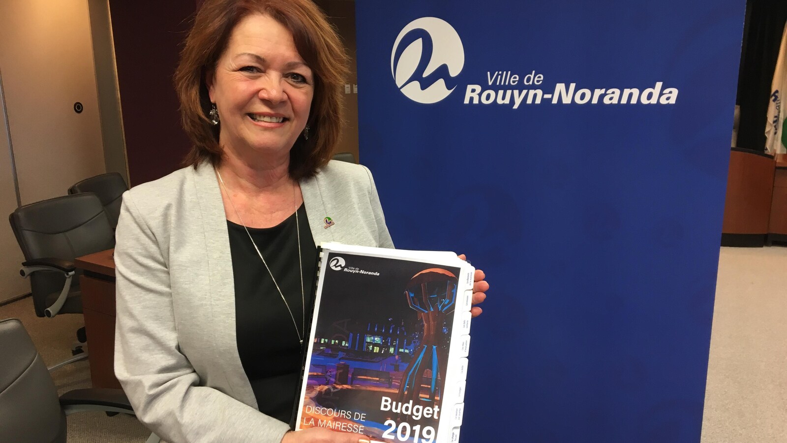 Diane Dallaire sourit à la caméra en tenant le document résumant le budget 2019 de Rouyn-Noranda.