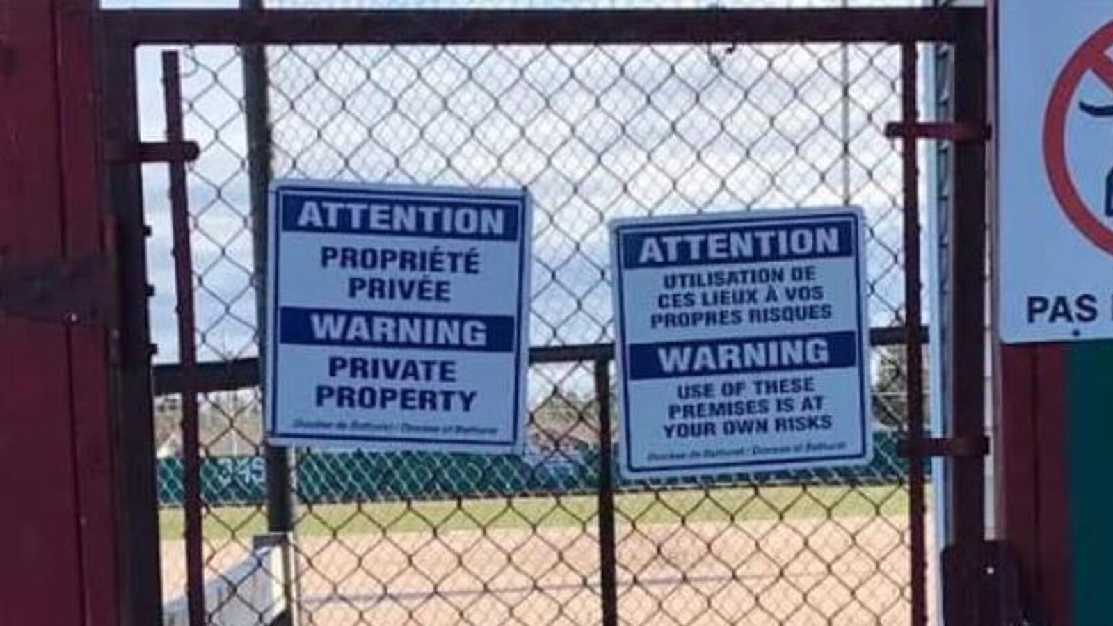On voit des affiches d'interdiction de passage sur un terrain de baseball public.