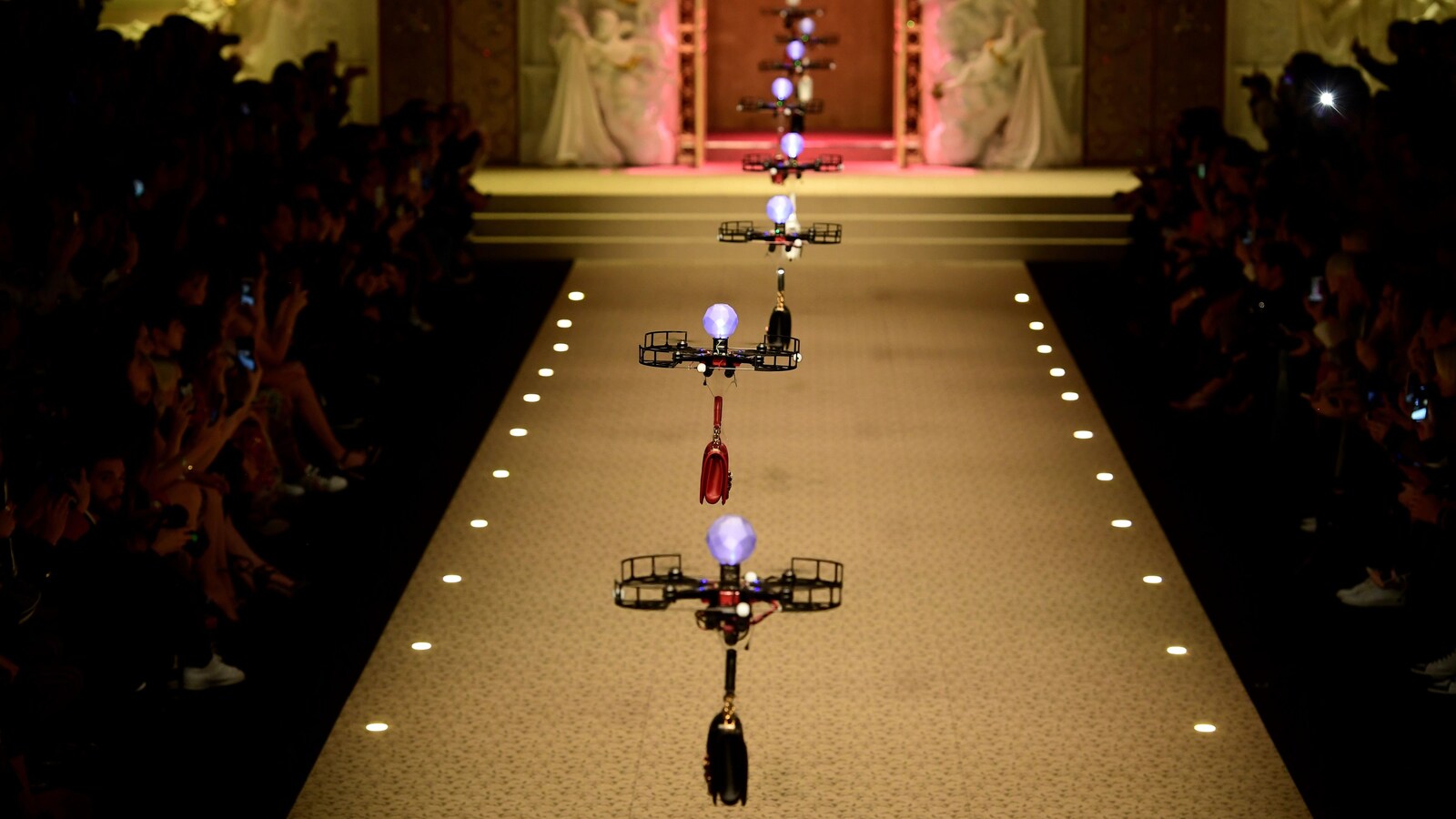 Des drones volent les uns derrière les autres au-dessus d'un podium, transportant des sacs à main.