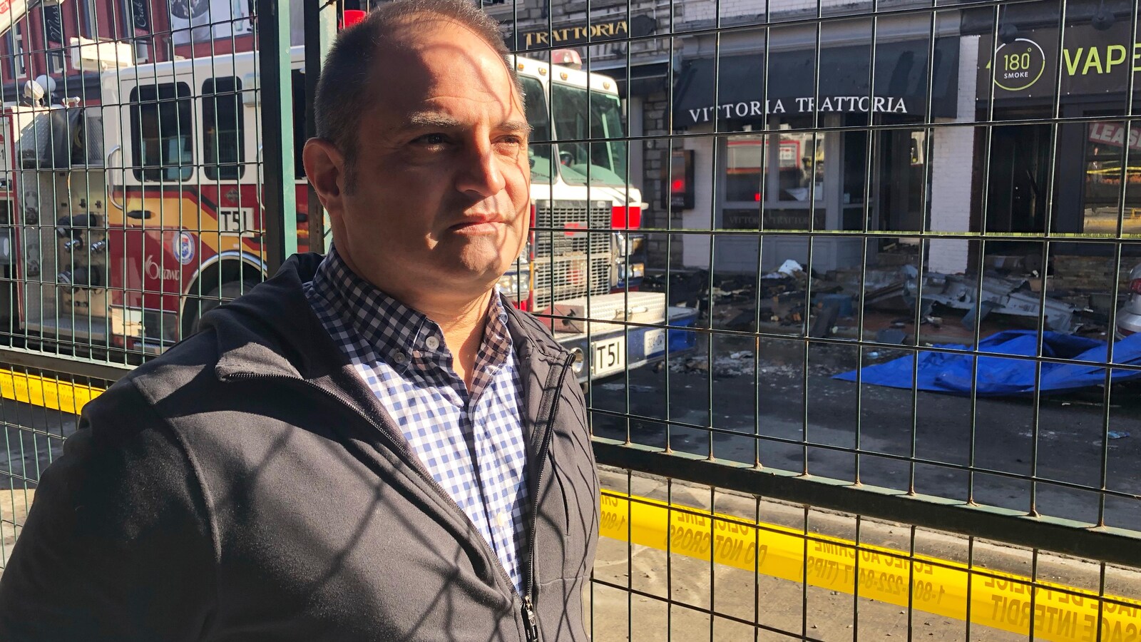 Domenic Santaguida pose pour une photo devant son restaurant détruit par un incendie. Un camion de pompiers est derrière lui.