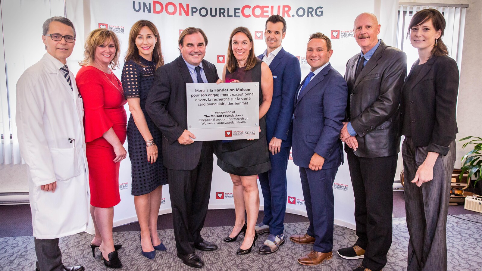 Des hommes et des femmes en costumes, en robes et en habits de médecin sourient. Un homme et un femme au milieu tiennent une plaque remerciant la Fondation Molson pour son don.
