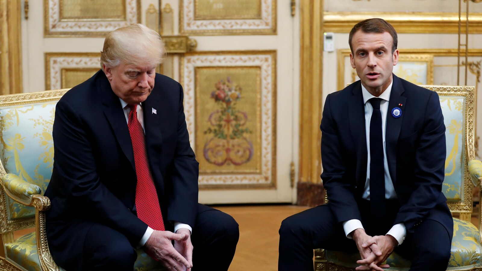 Trump et Macron sont assis côte à côte, Trump regarde par terre.