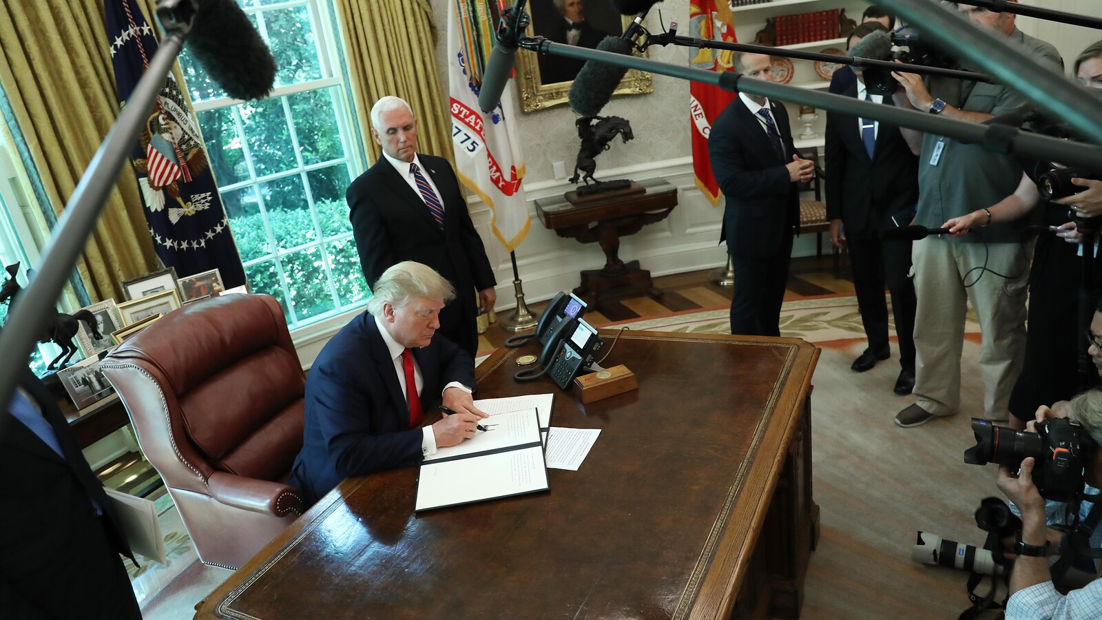 Donald Trump signe un document dans son bureau de la Maison-Blanche devant plusieurs journalistes.