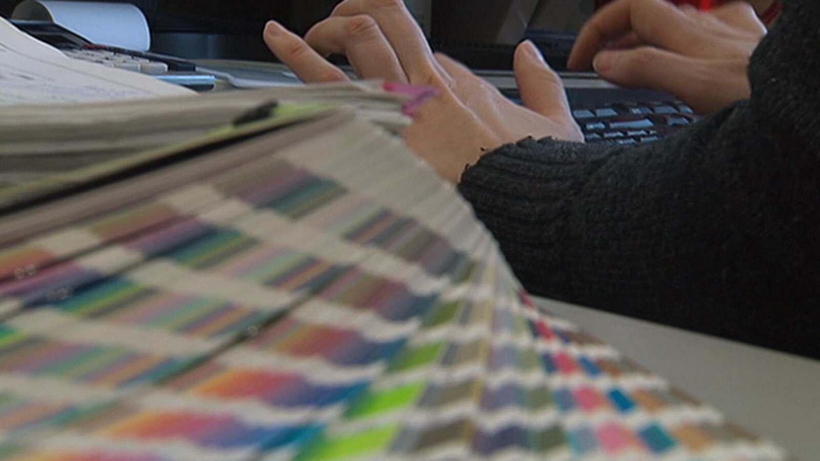 Une personne tape sur un clavier d'ordinateur, une pile de dossiers est déposée sur son bureau.