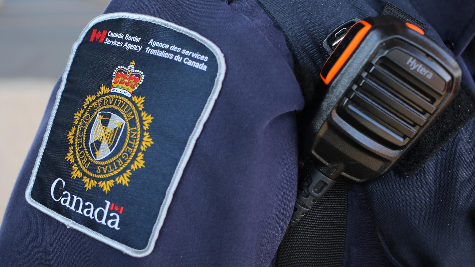 On voit la manche de l'uniforme d'un agent frontalier.