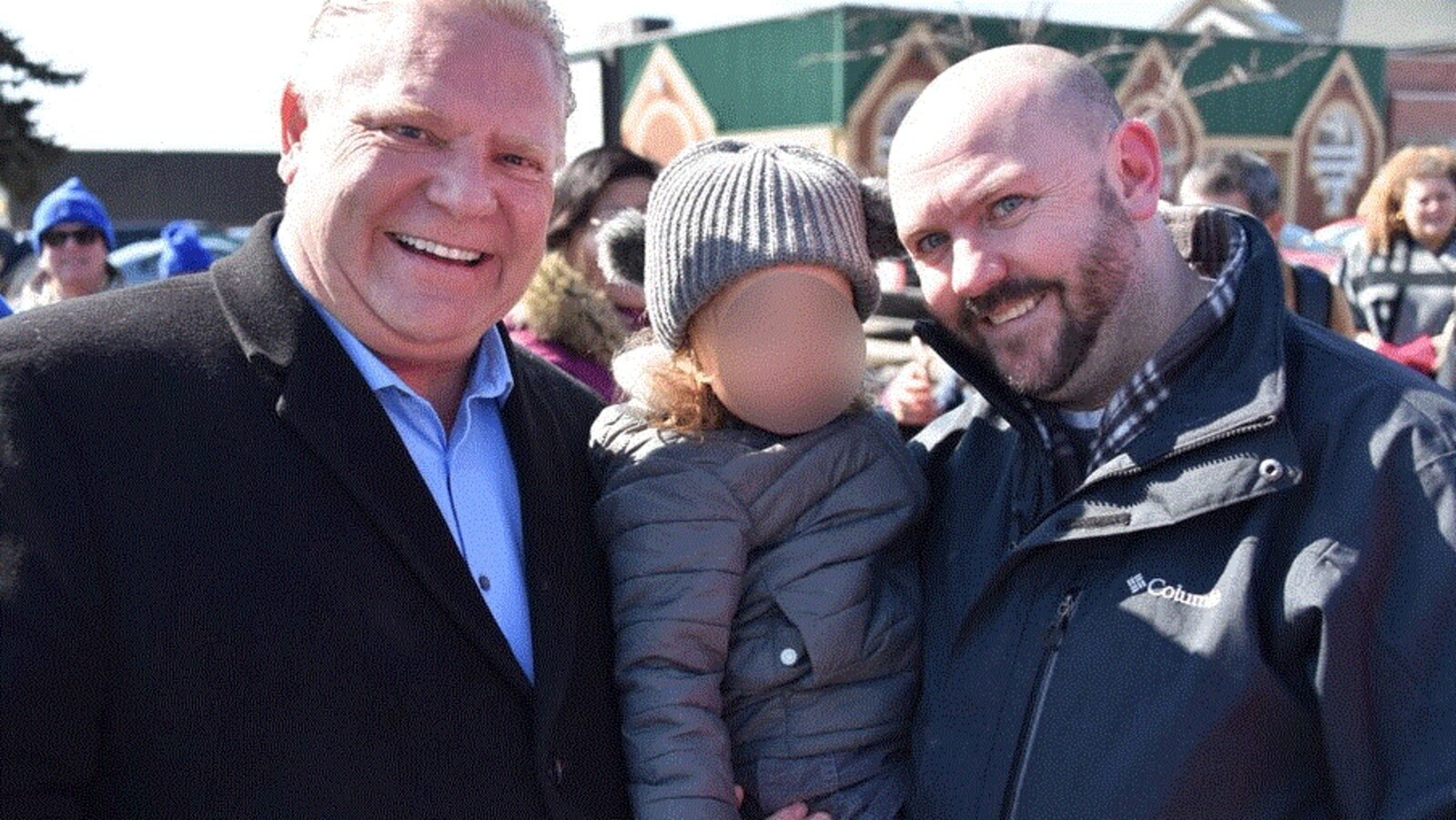 Photo de deux hommes l'un à côté de l'autre à l'extérieur. L'un des hommes tient un enfant dans les bras.