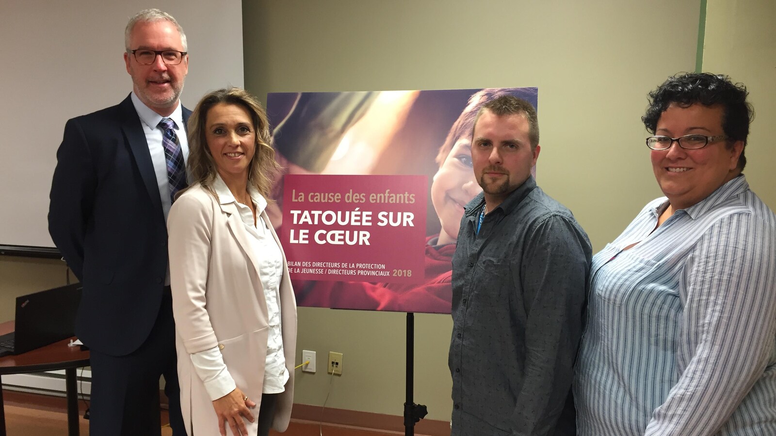Deux hommes et deux femmes posent autour d'Une affiche disant «La cause des enfants tatouée sur le coeur».
