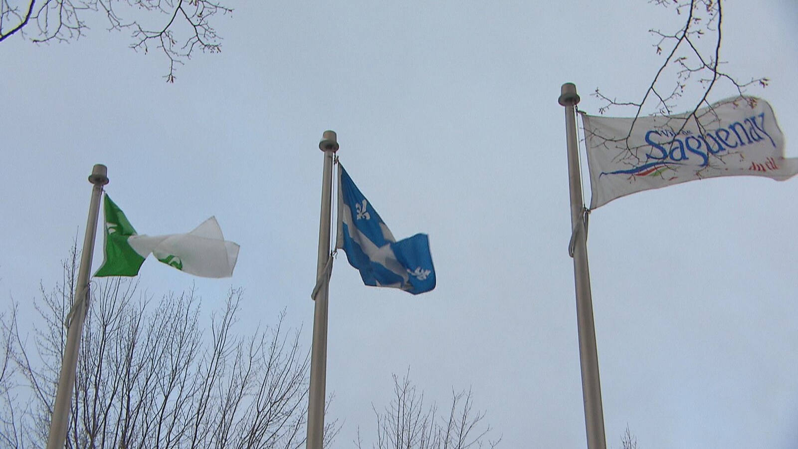 Trois mâts avec trois drapeaux : Celui de la communauté franco-ontarienne, celui du Québec et celui de la Ville de Saguenay.