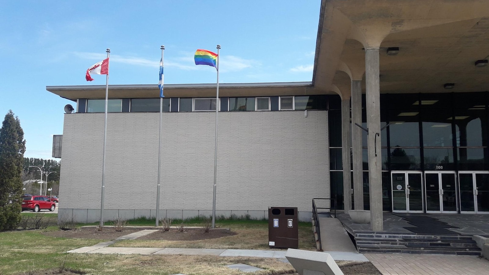 Devant l'hôtel de ville de Dolbeau-Mistassini, trois drapeaux flottent au vent.