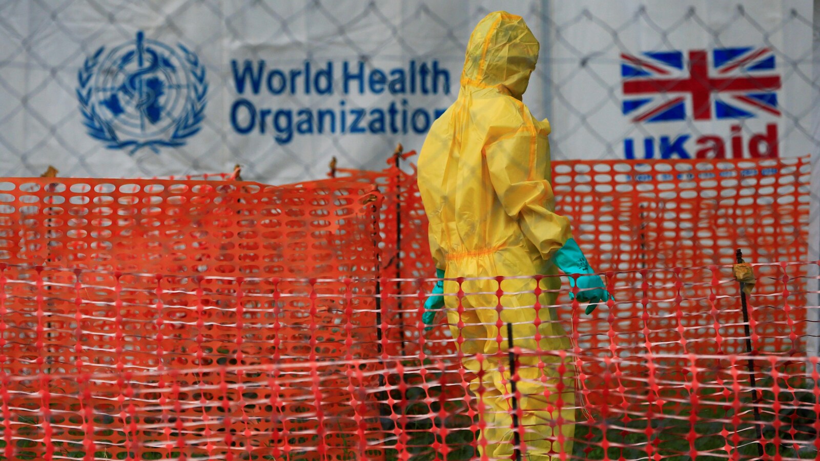 Une personne, vêtue d'une combinaison protectrice, se trouve devant une tente de l'Organisation mondiale de la santé.