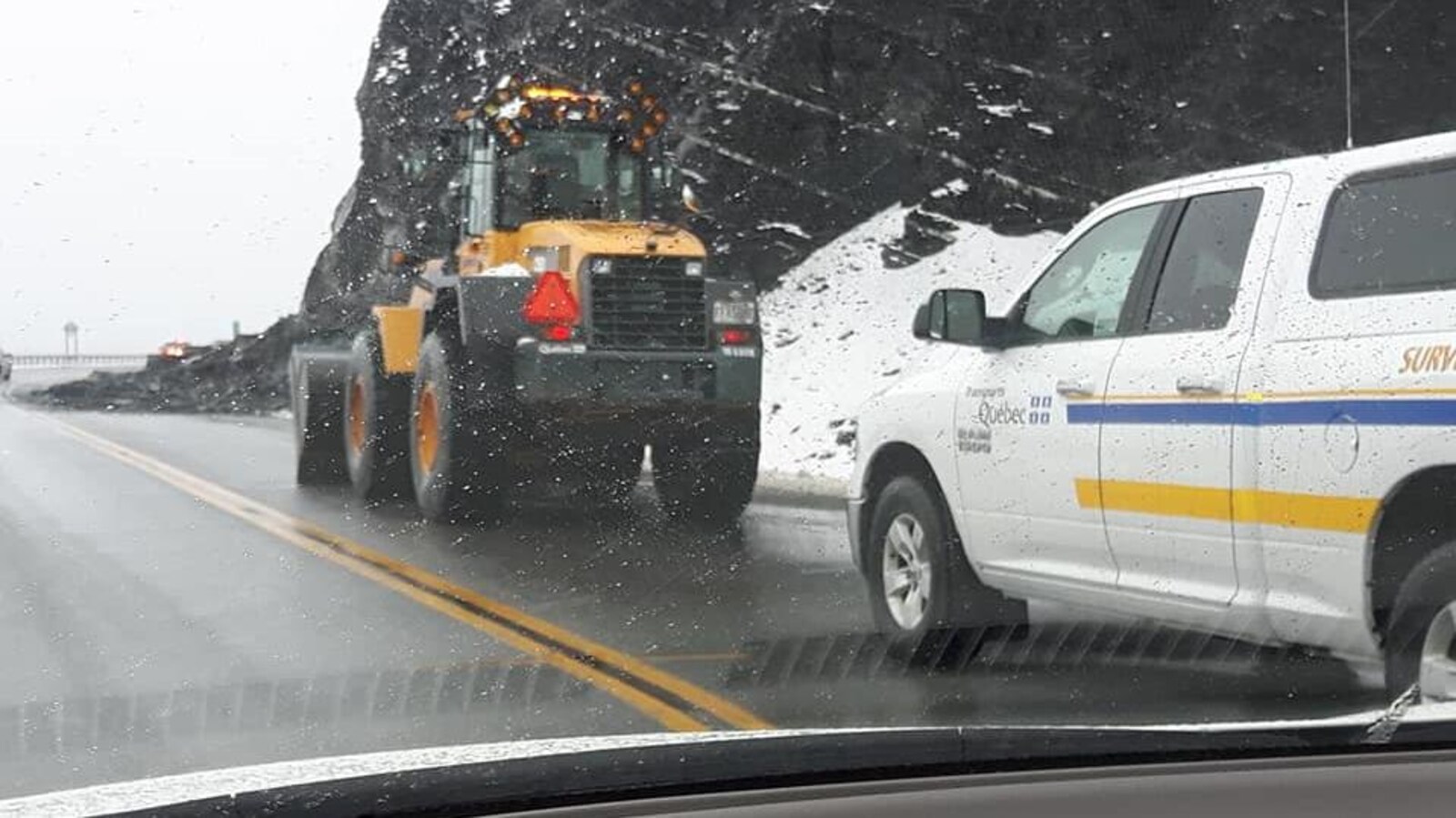 Un tracteur et une voiture du MTQ devant une falaise.
