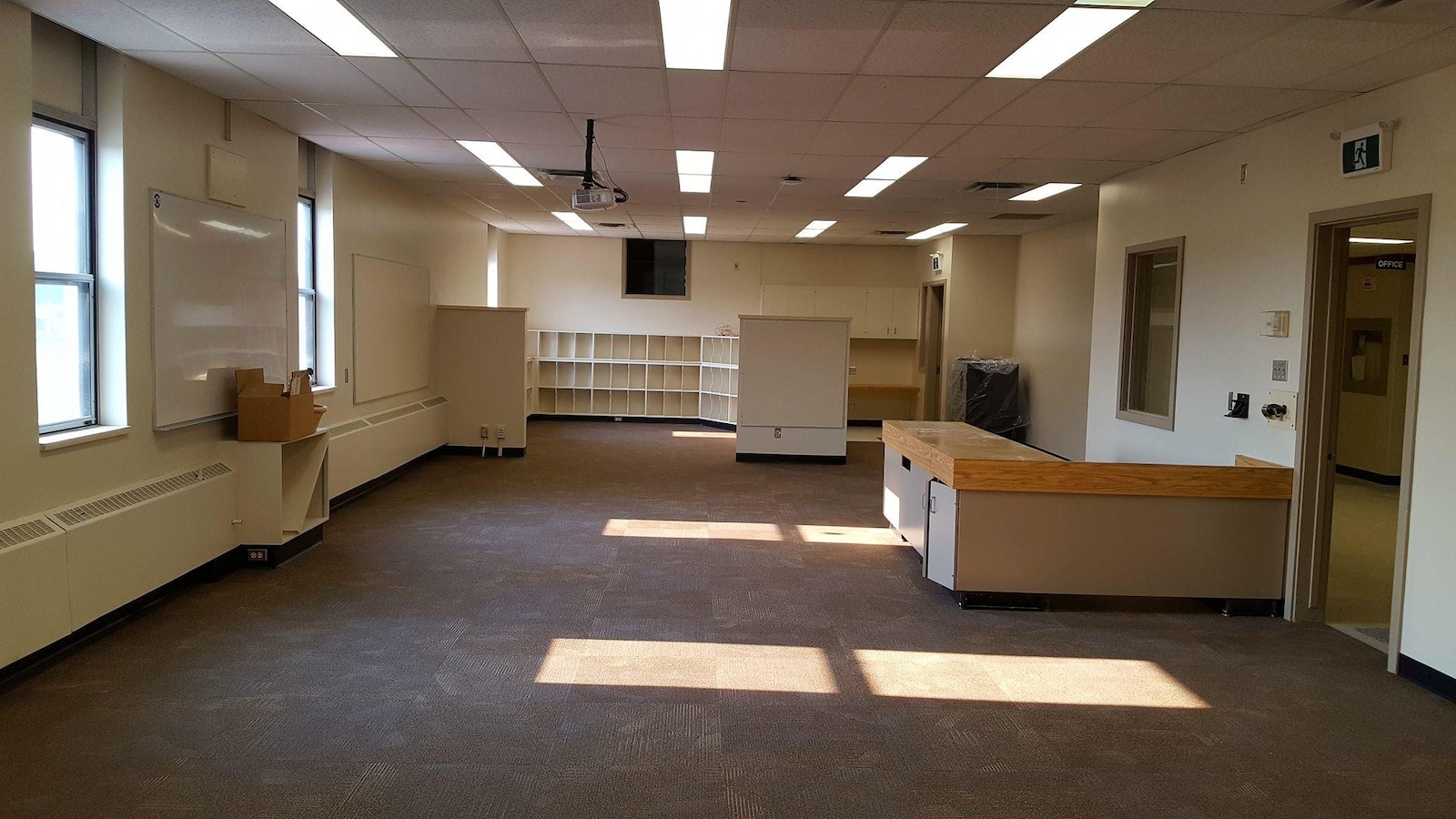 Une pièce scolaire vide avec des bureaux et des étagères.