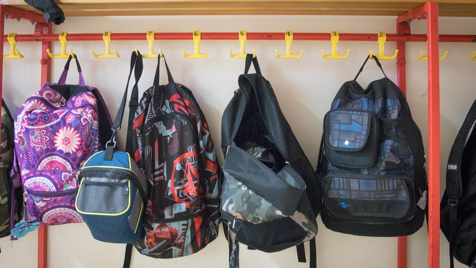 Des sacs à dos d'élèves accrochés sur un mur