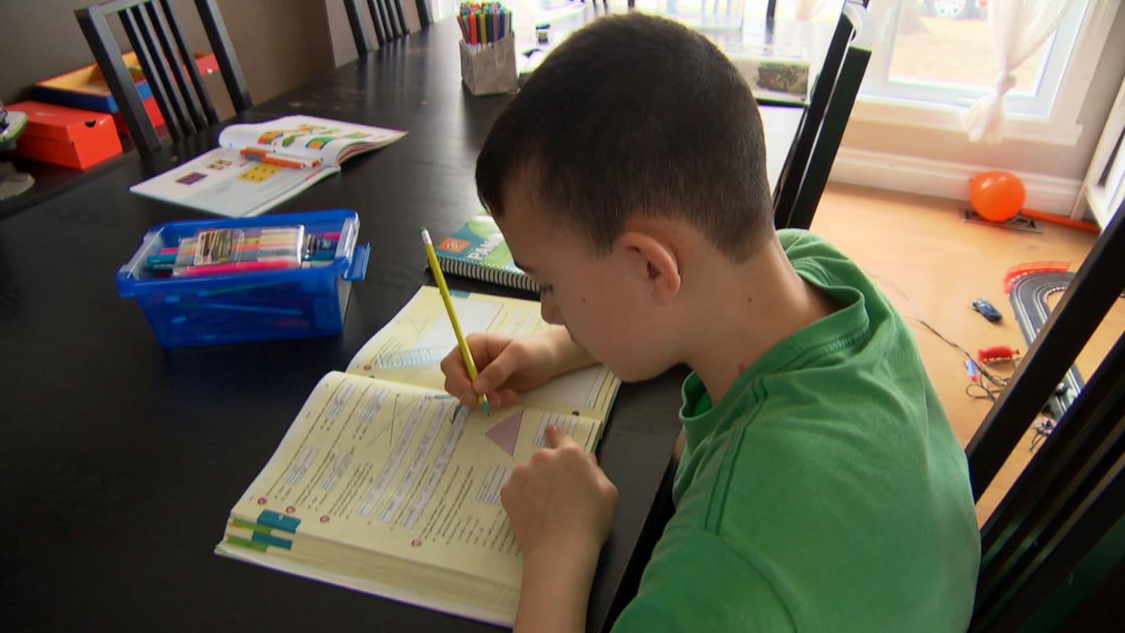 Un jeune garçon fait ses devoirs sur la table de la maison familiale.