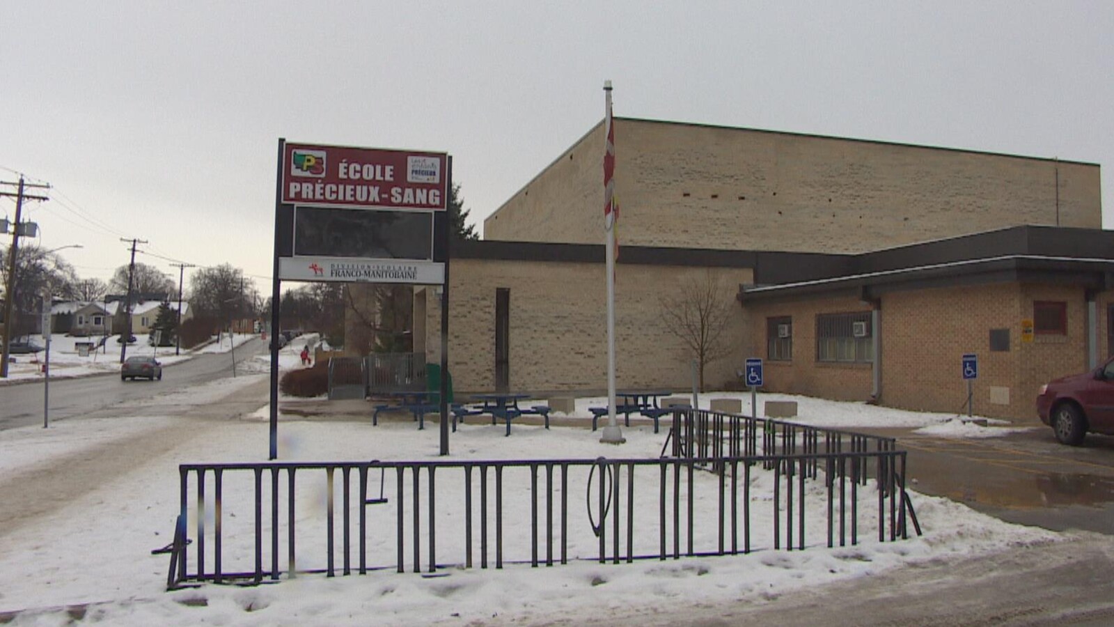L'école, vue de loin, un jour de neige. Un grand panneau annonce : « ÉCOLE PRÉCIEUX-SANG ».