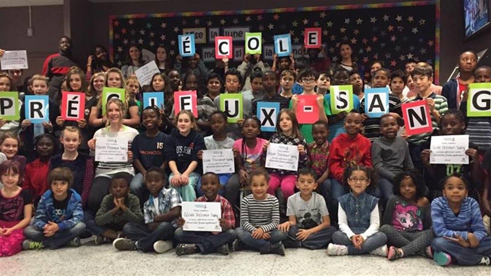 Les élèves de l'école Précieux-Sang tiennent des feuilles avec des lettres qui composent le nom de leur école.