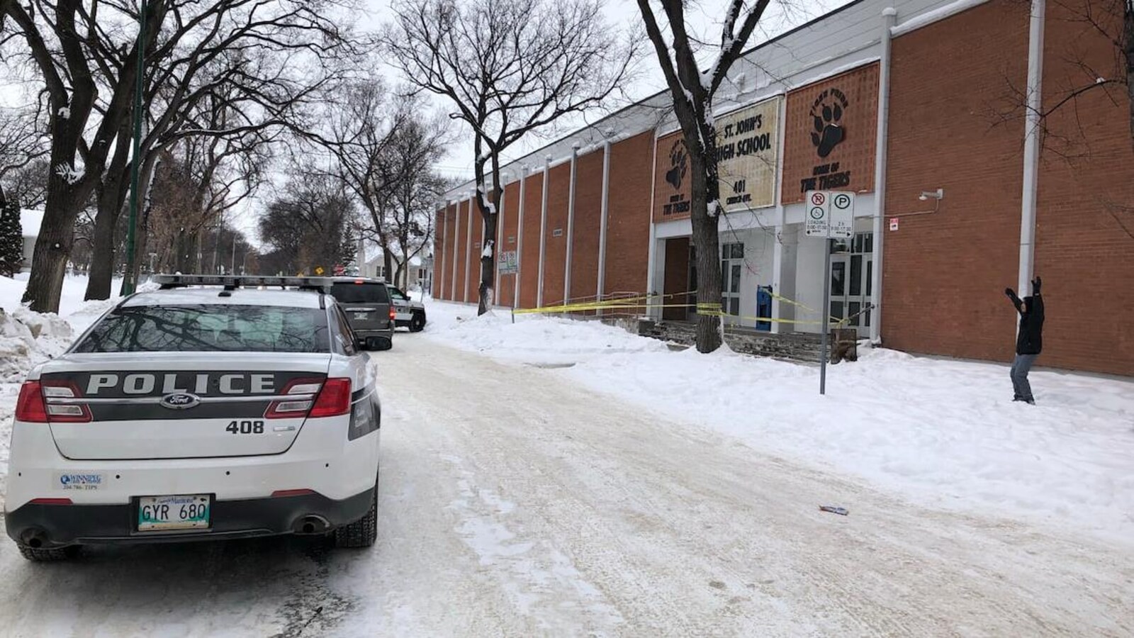 Des voitures de police sont stationnées sur la rue, devant une école.