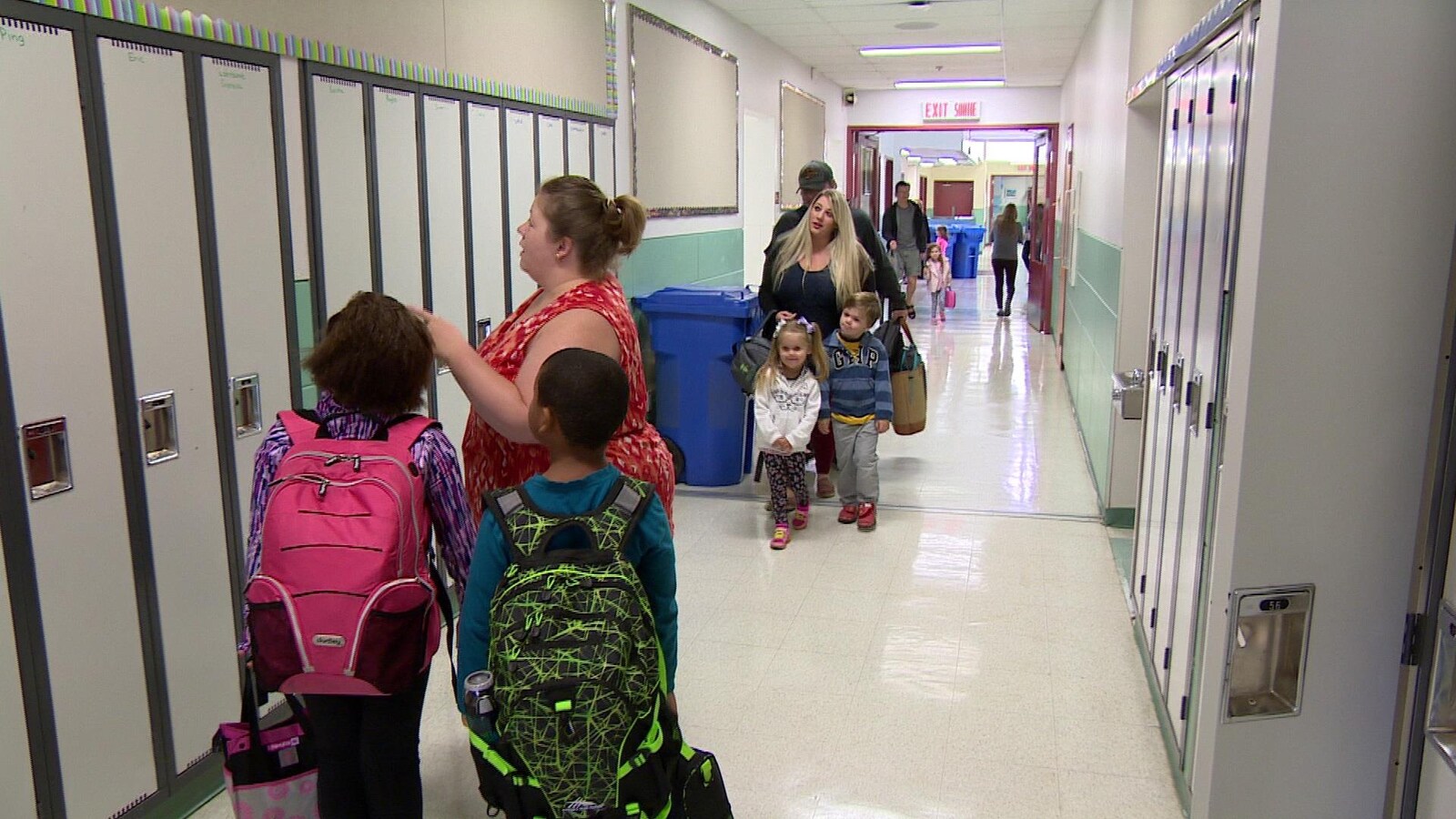 Une enseignante montre un casier à deux jeunes élèves, alors que des parents accompagnent leurs enfants à leur classe.