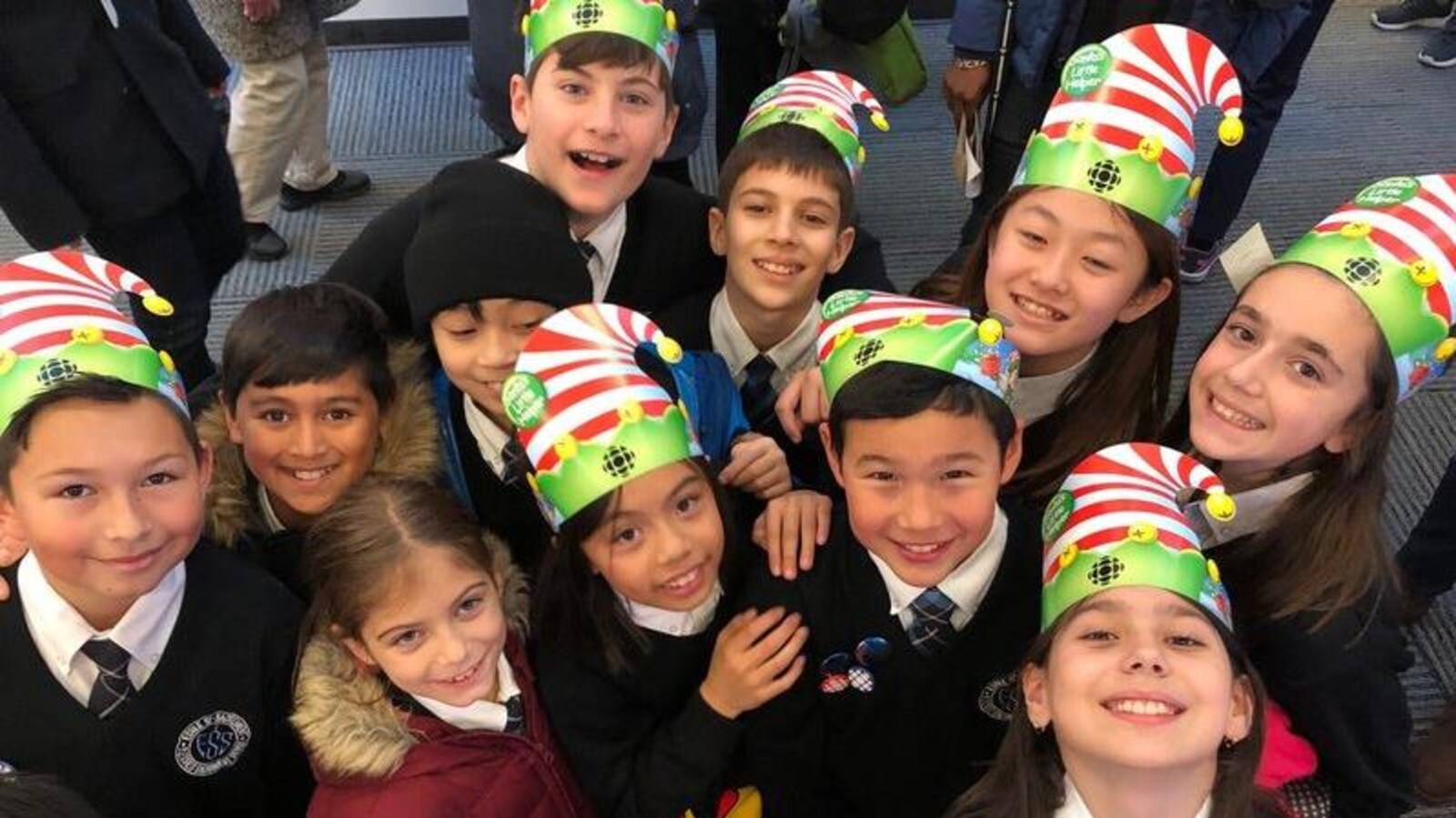 Des écoliers souriants et portant un uniforme dans la salle de nouvelles de Radio-Canada lèvent ensemble la tête vers l'appareil photo.