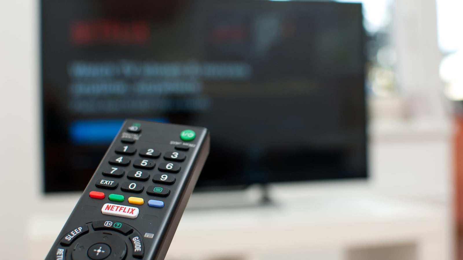 Une télécommande avec un bouton netflix pointe vers un écran de télévision.