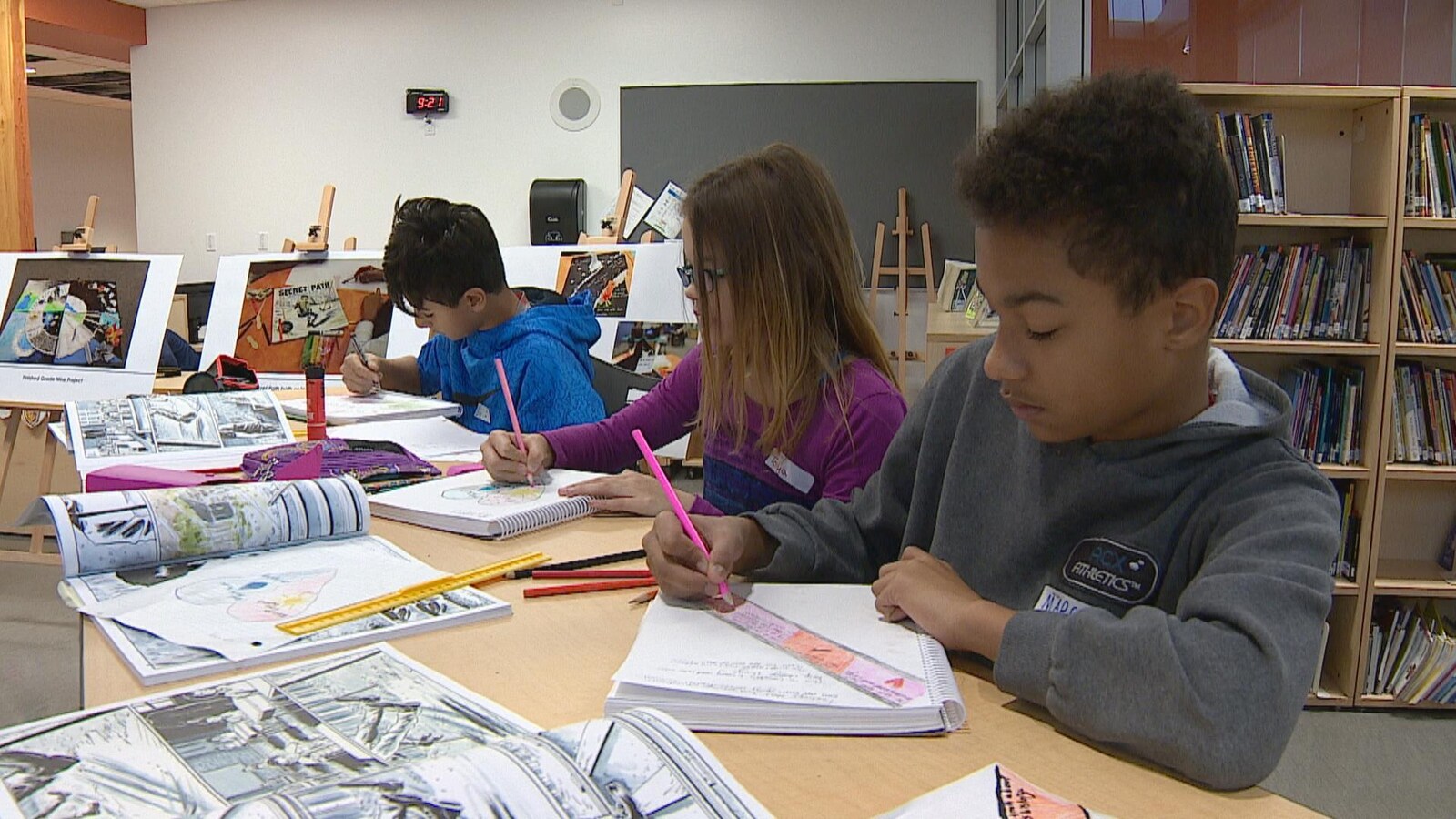Trois enfants écrivent dans des cahiers, entourés de ressources pédagogiques.