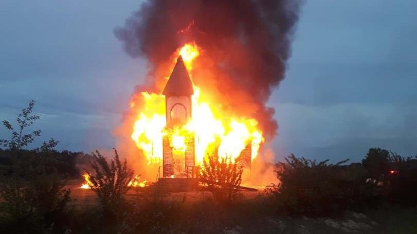Une église complètement en feu, un énorme nuage de fumée épaisse est au dessus de celle-ci.