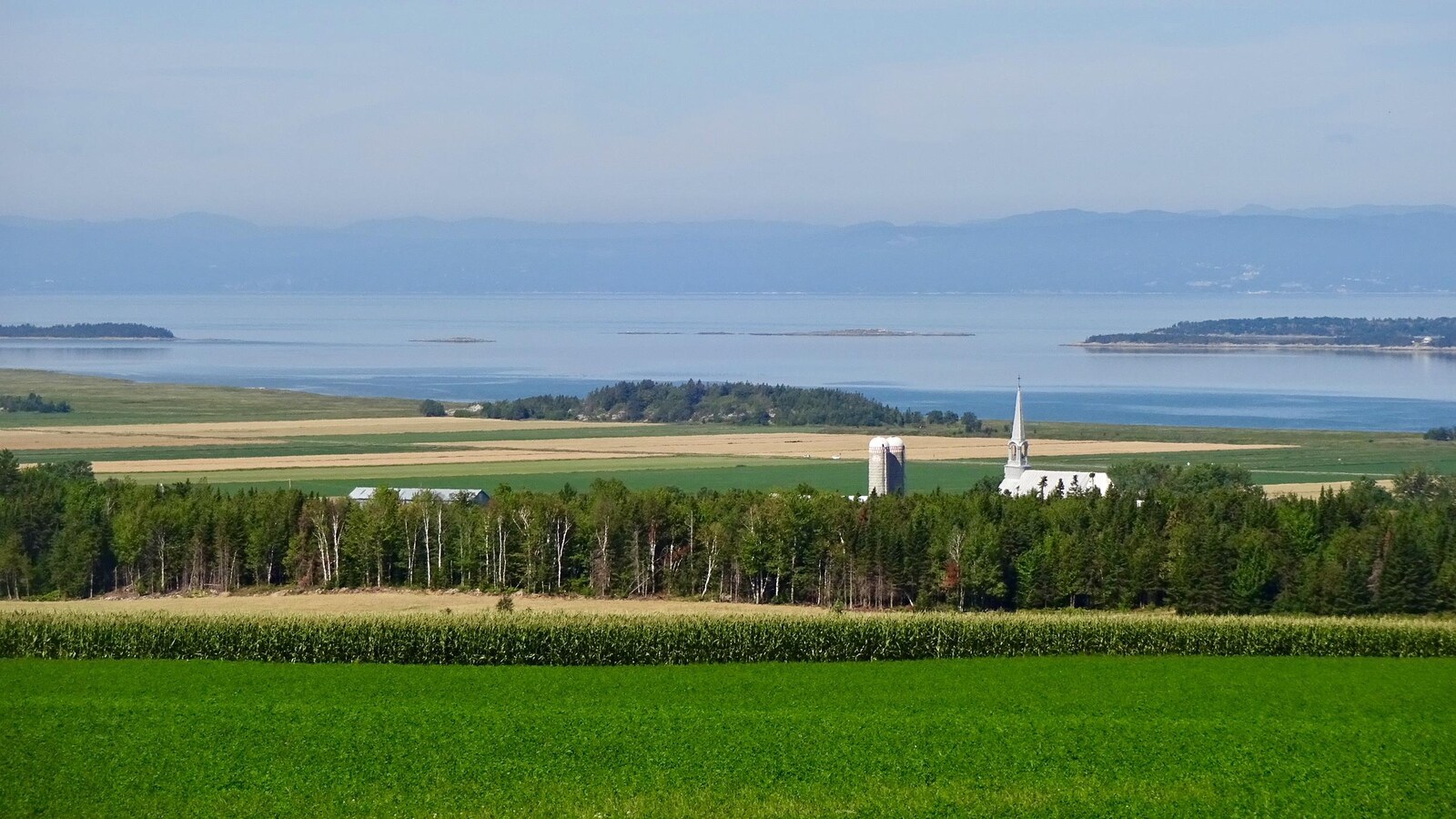 L'église de Saint-Germain-de-Kamouraska, à travers champs, avec le fleuve et Charlevoix en arrière plan.