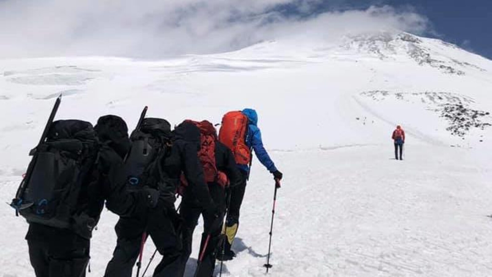 Des alpinistes grimpent vers le sommet enneigé d'une montagne.