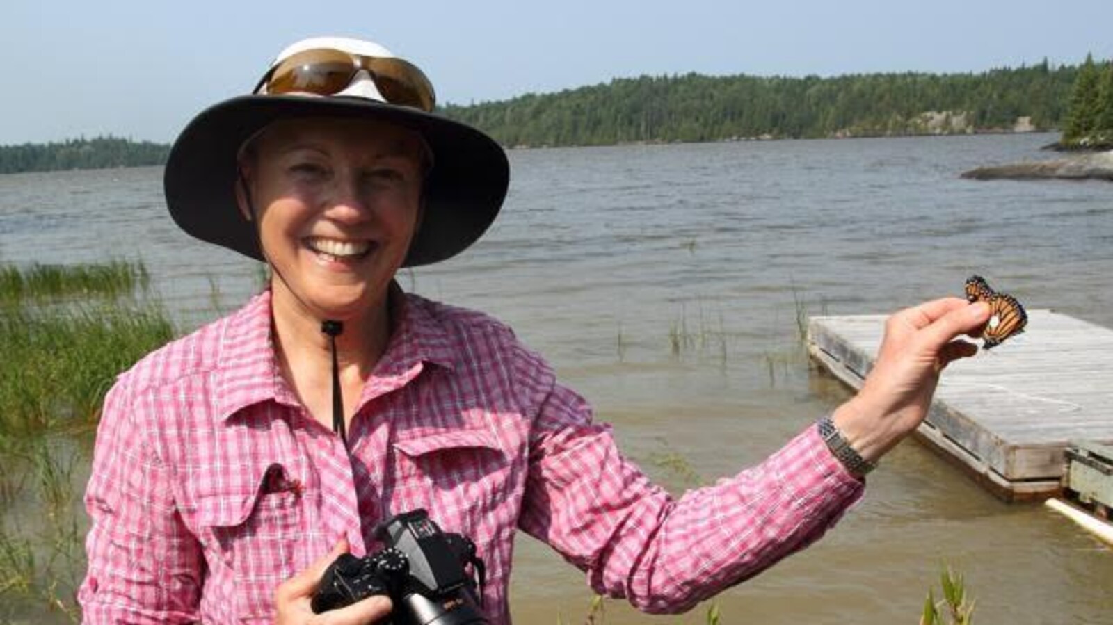 Une femme tenant un monarque devant un lac.