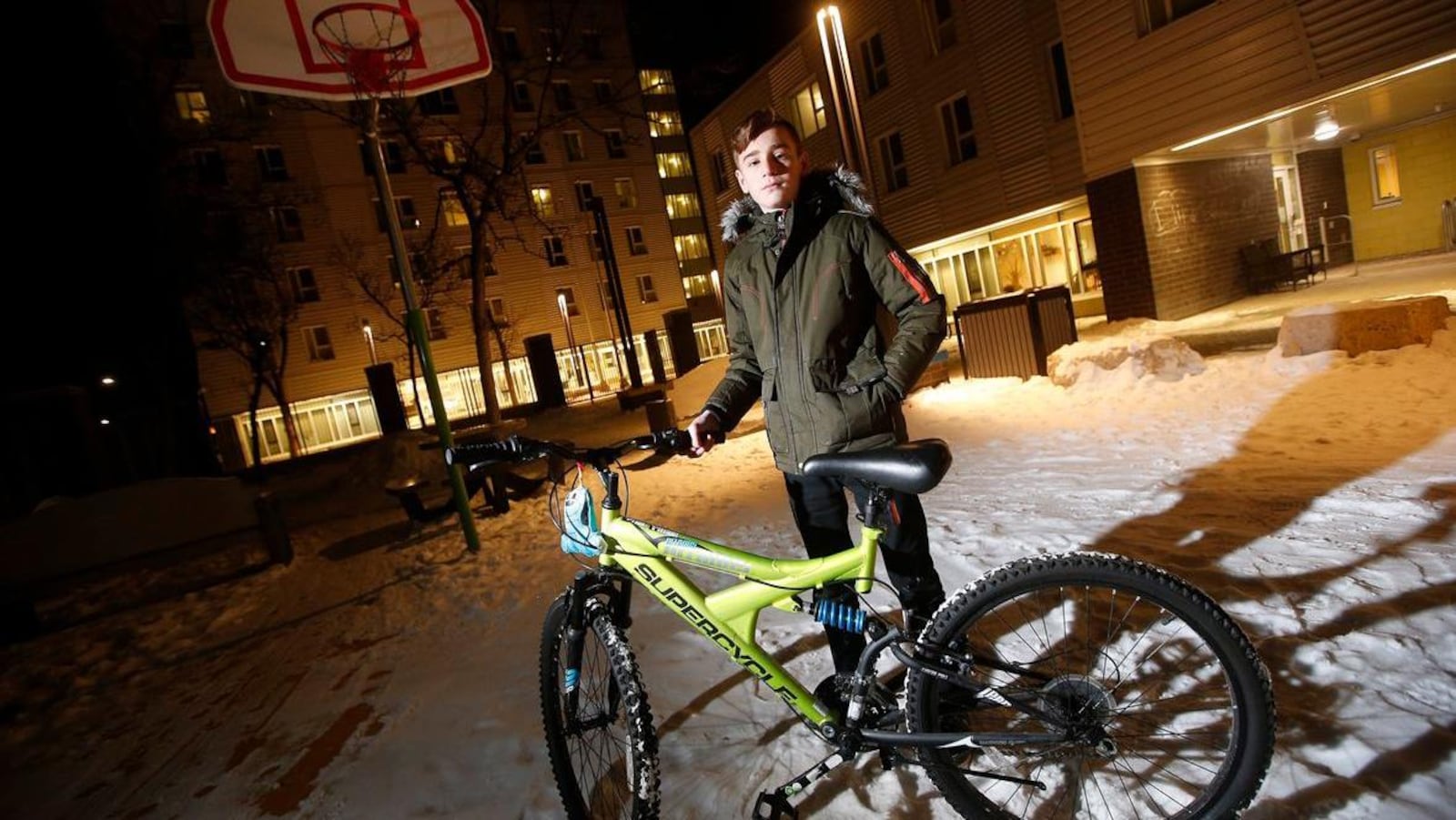 Emad Tamo tient le guidon d'un vélo debout dans la neige devant un immeuble.