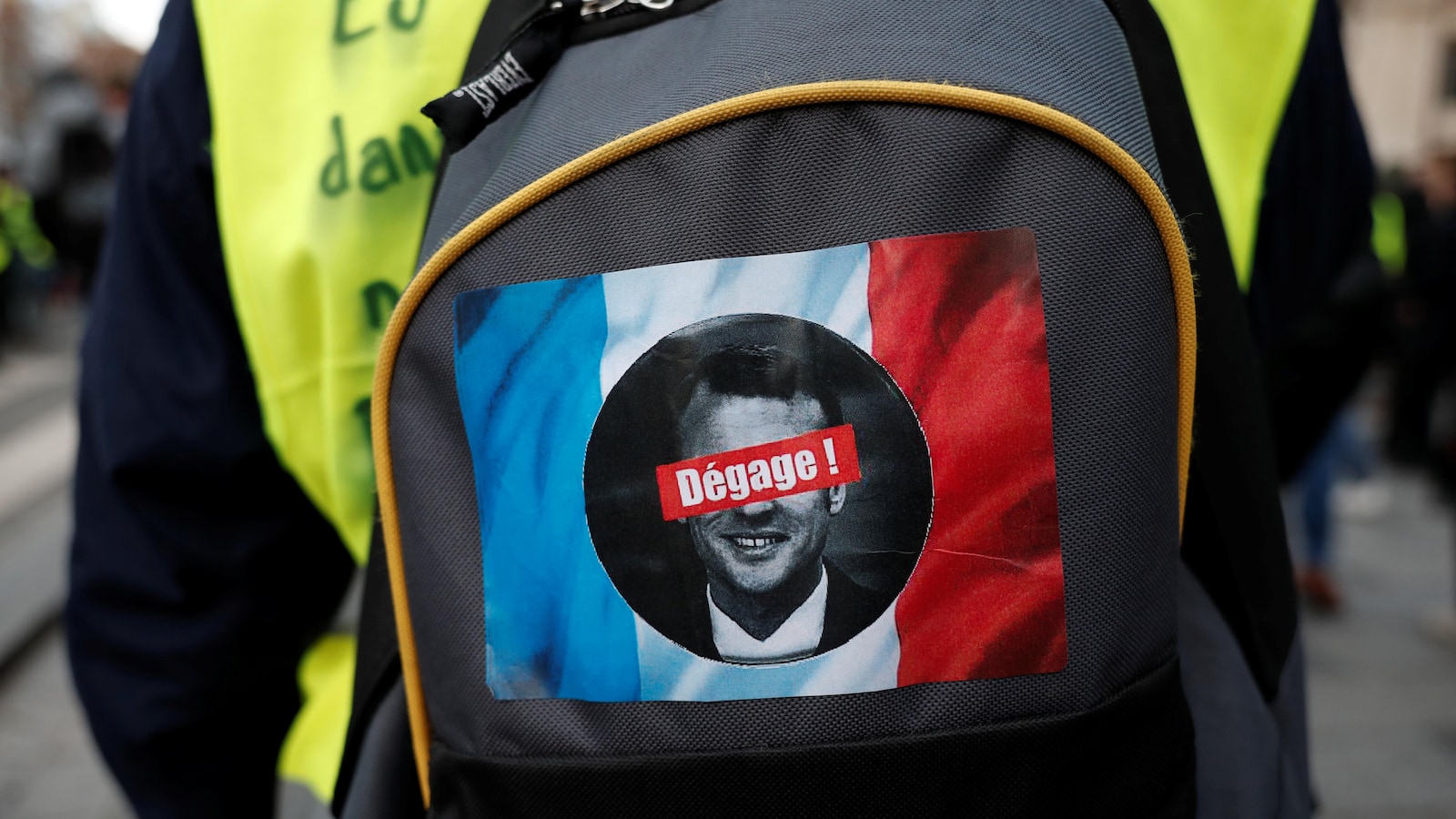 Un autocollant affichant le mot dégage sur le visage d'Emmanuel Macron se trouve sur le sac-à-dos d'une manifestante.