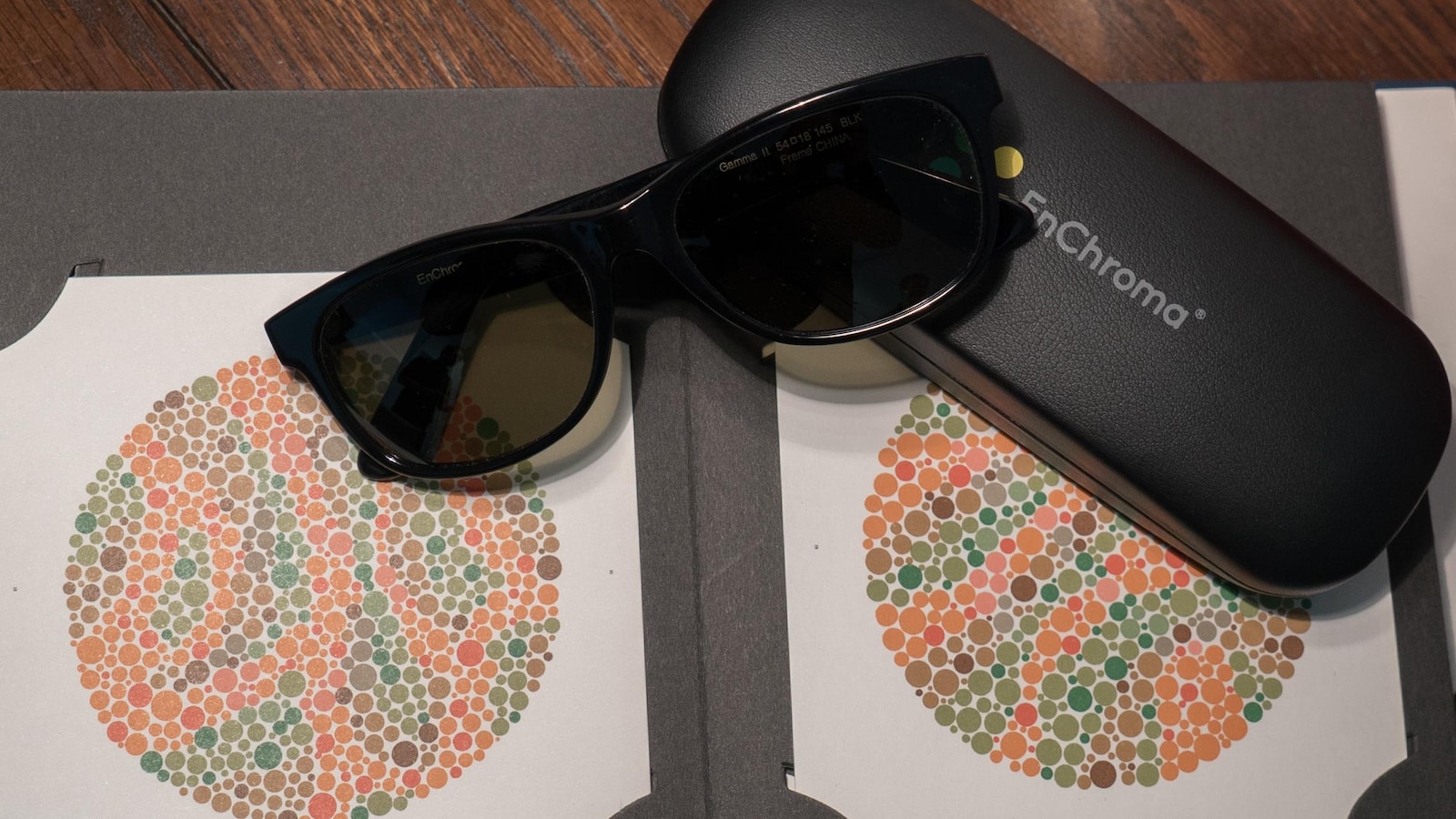Une paire de lunettes foncées EnChroma déposées sur son étui et sur deux cercles d'un test d'Ishihara.