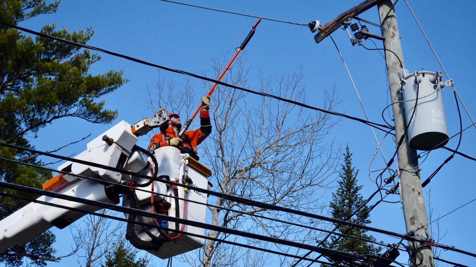 Un travailleur d'Énergie NB, dans une nacelle, tente de réparer une ligne électrique.