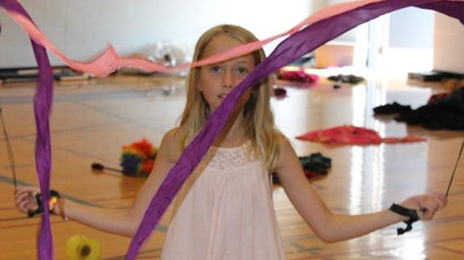 Une jeune fille d'environ 10 ans, dans une salle de sport, en fait tourner les rubans de ses bolas devant elle.